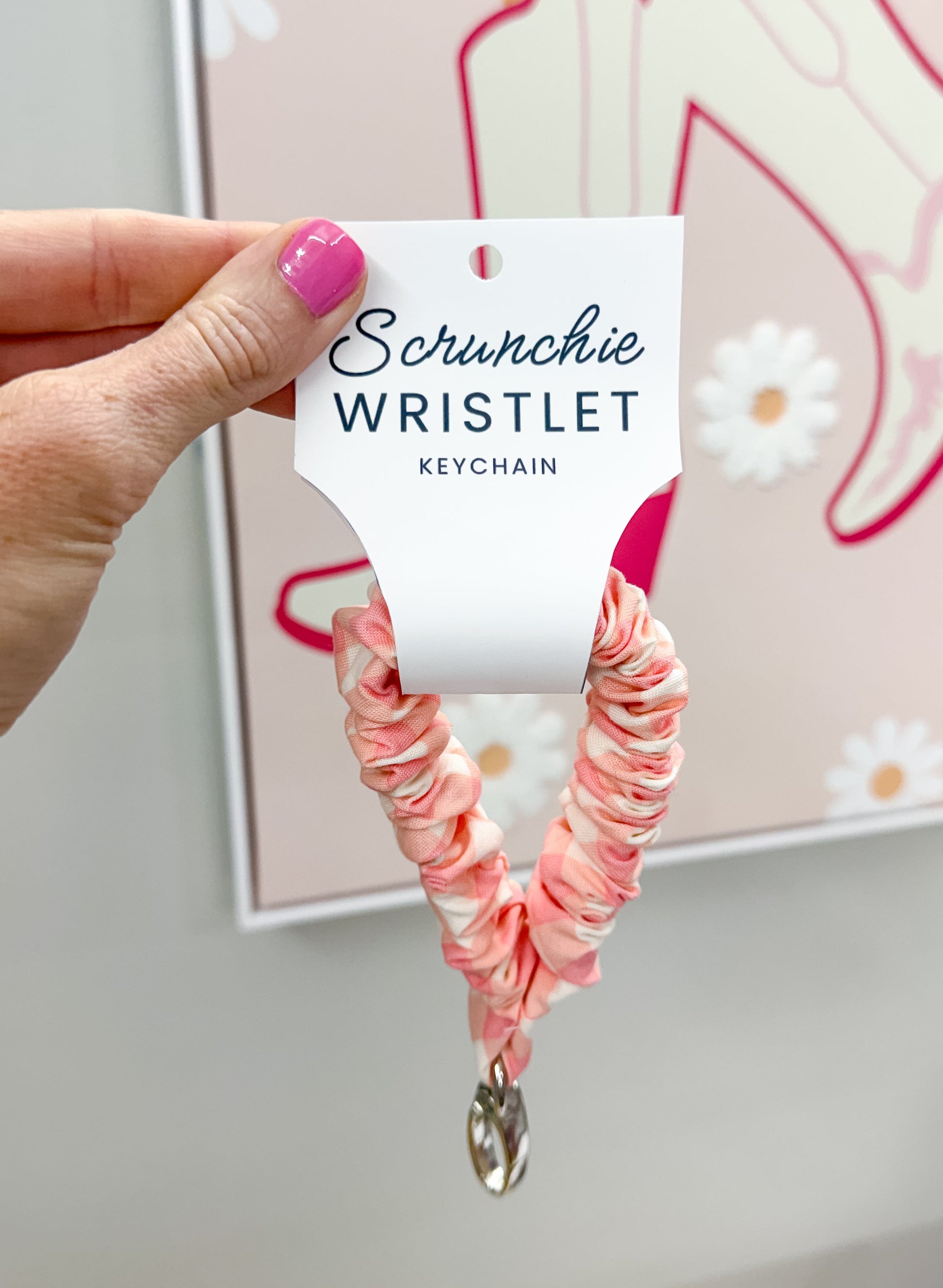Pink scrunchie wristlet held by a hand with a blurred background