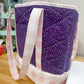 Purple quilted bag with pink handles on a wooden surface