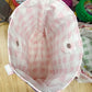 Pink checkered baby hat on a wooden surface with a cluttered background