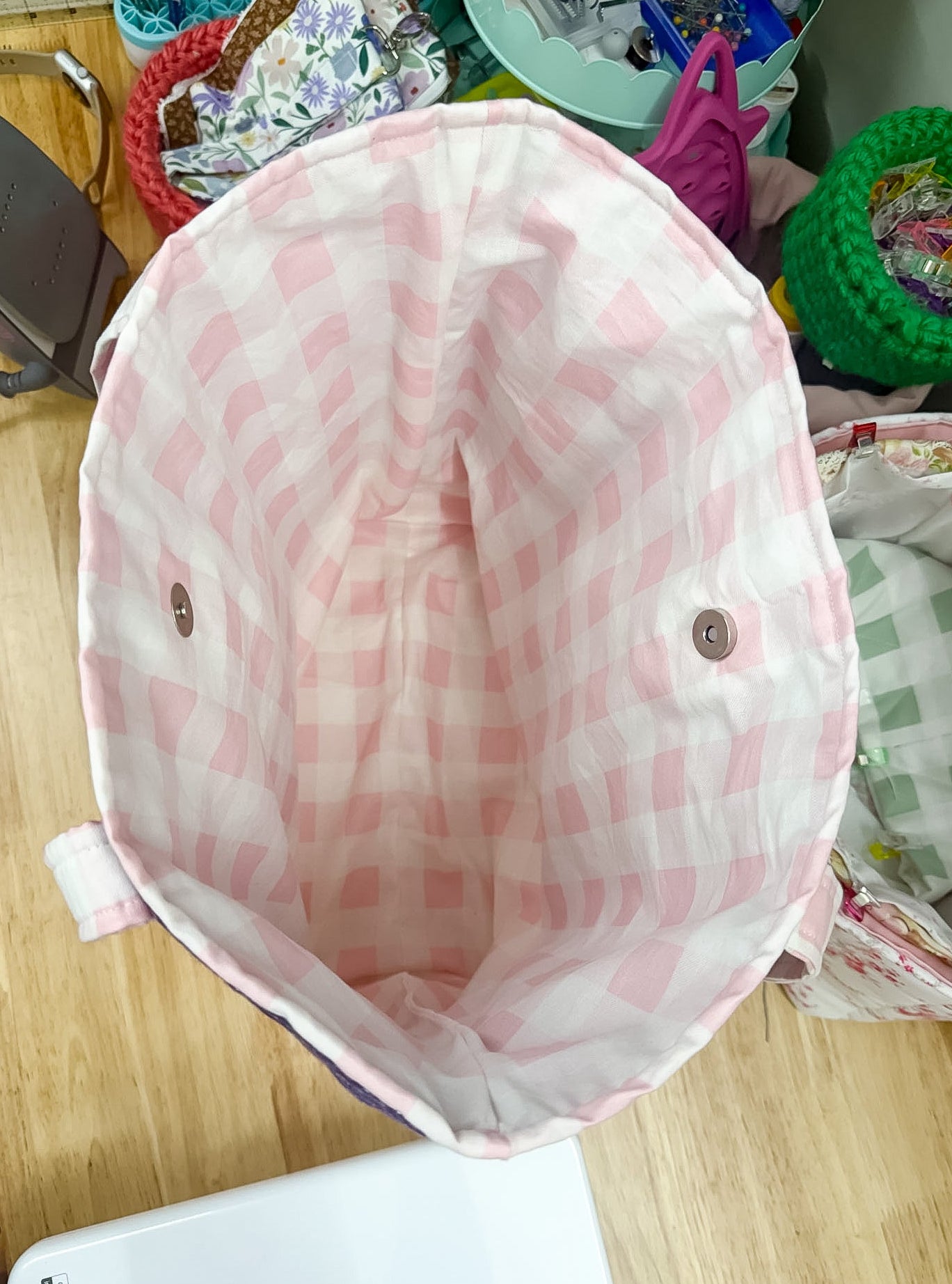 Pink checkered baby hat on a wooden surface with a cluttered background