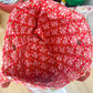 Red floral-patterned fabric on a wooden surface with various items in the background.