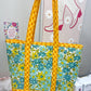 Yellow and floral-patterned tote bag on a sewing machine with a sewing-themed wall art in the background.