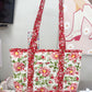 Floral-patterned tote bag held by a person with sewing machine and fabric in the background