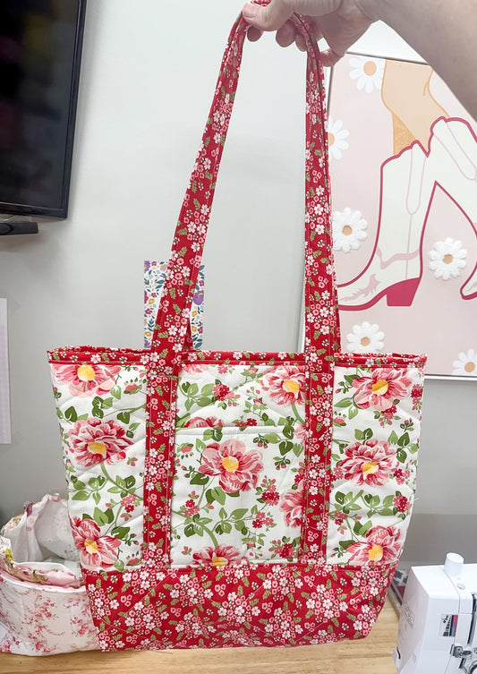 Floral-patterned tote bag held by a person with sewing machine and fabric in the background