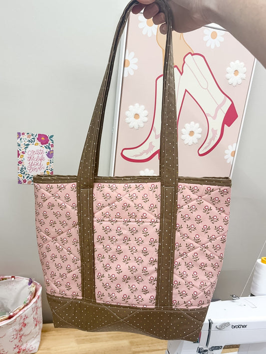 Handmade tote bag with pink floral pattern held above a sewing machine.