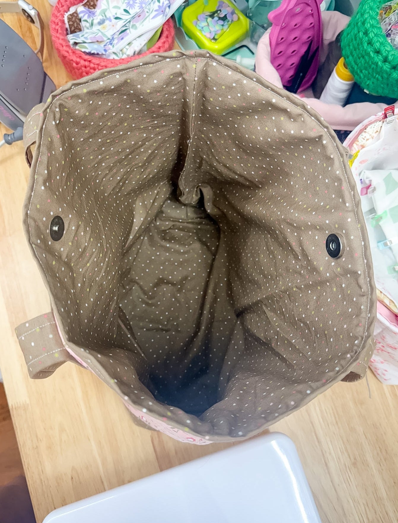 Brown fabric bag with black buttons on a wooden surface with various items in the background
