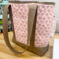 Pink floral-patterned bag with brown handle and trim on a wooden table.