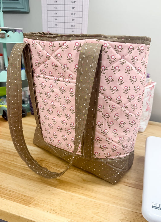 Pink floral-patterned bag with brown handle and trim on a wooden table.