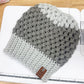 Gray and white knitted beanie on a white surface with a ruler for scale.