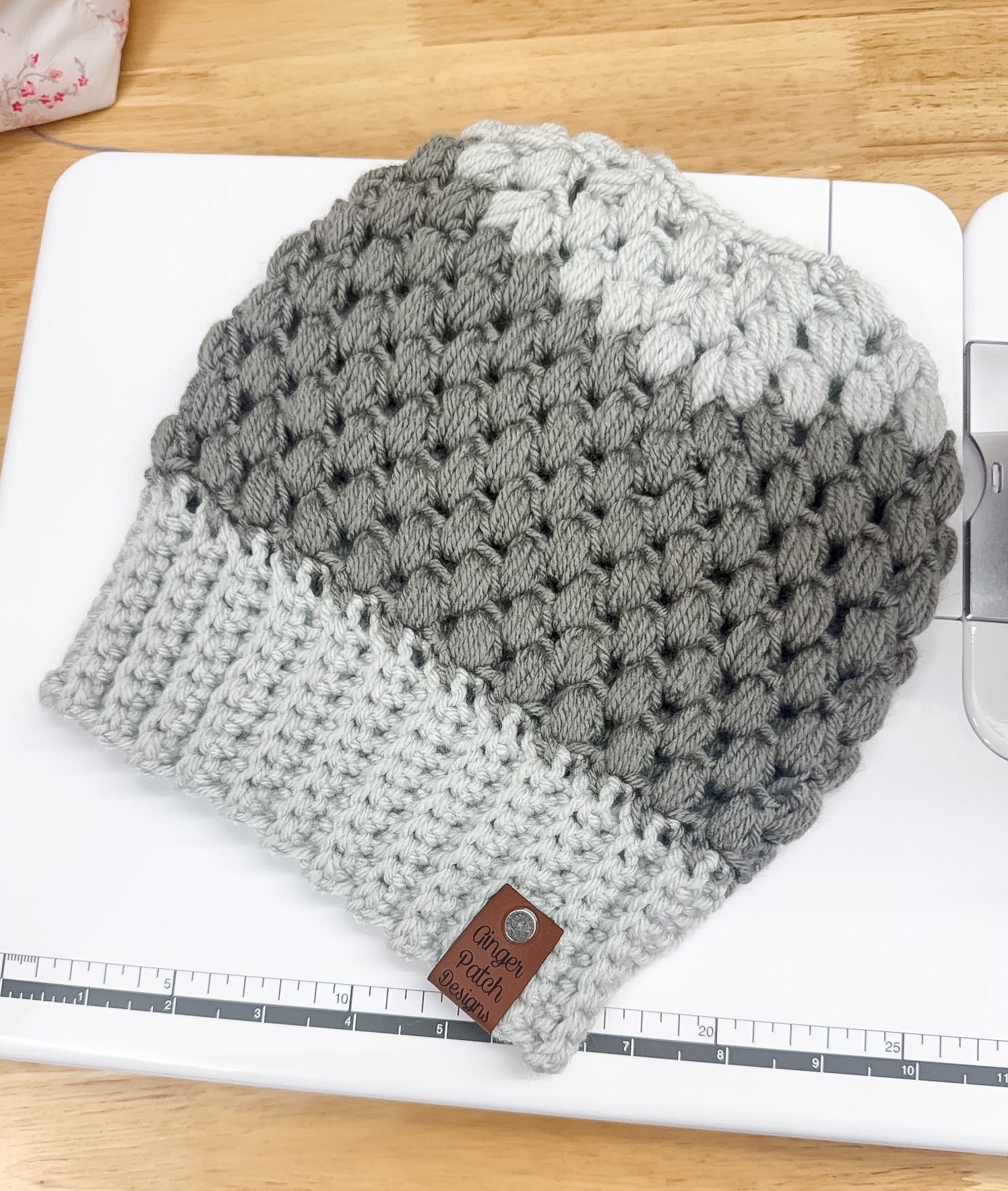 Gray and white knitted beanie on a white surface with a ruler for scale.