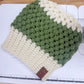 Green and white crocheted beanie with a brown leather tag on a white surface.