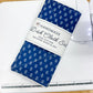A folded dishcloth set wrapped in a white paper band labeled 'HANDMADE Dishcloth Set 100% COTTON MACHINE WASH & DRY,' placed on a white sewing machine over a light wood surface.