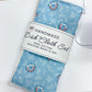 A handmade dish cloth set in a light blue floral print, wrapped in a white paper band label and placed on top of a white sewing machine over a wooden table.