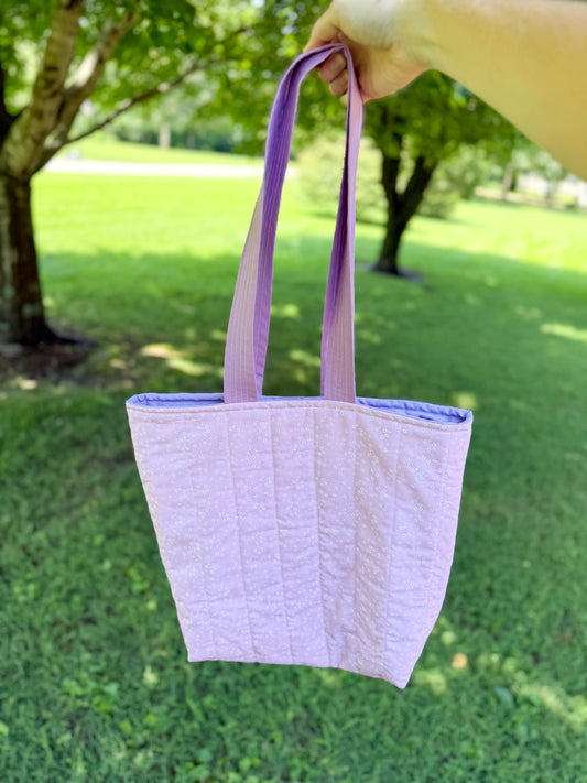 Purple tote bag held by a hand with a grassy background