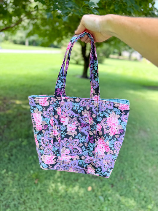 Floral patterned tote bag held by a hand outdoors on grass