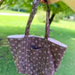 Person holding a floral-patterned tote bag outdoors with green grass and trees in the background