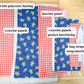 A flat lay of fabric panels and white elastic straps on a light wood surface, labeled with white text boxes identifying components such as exterior panels, interior panel, high loft polyester batting, and bag straps plus strap interfacing.