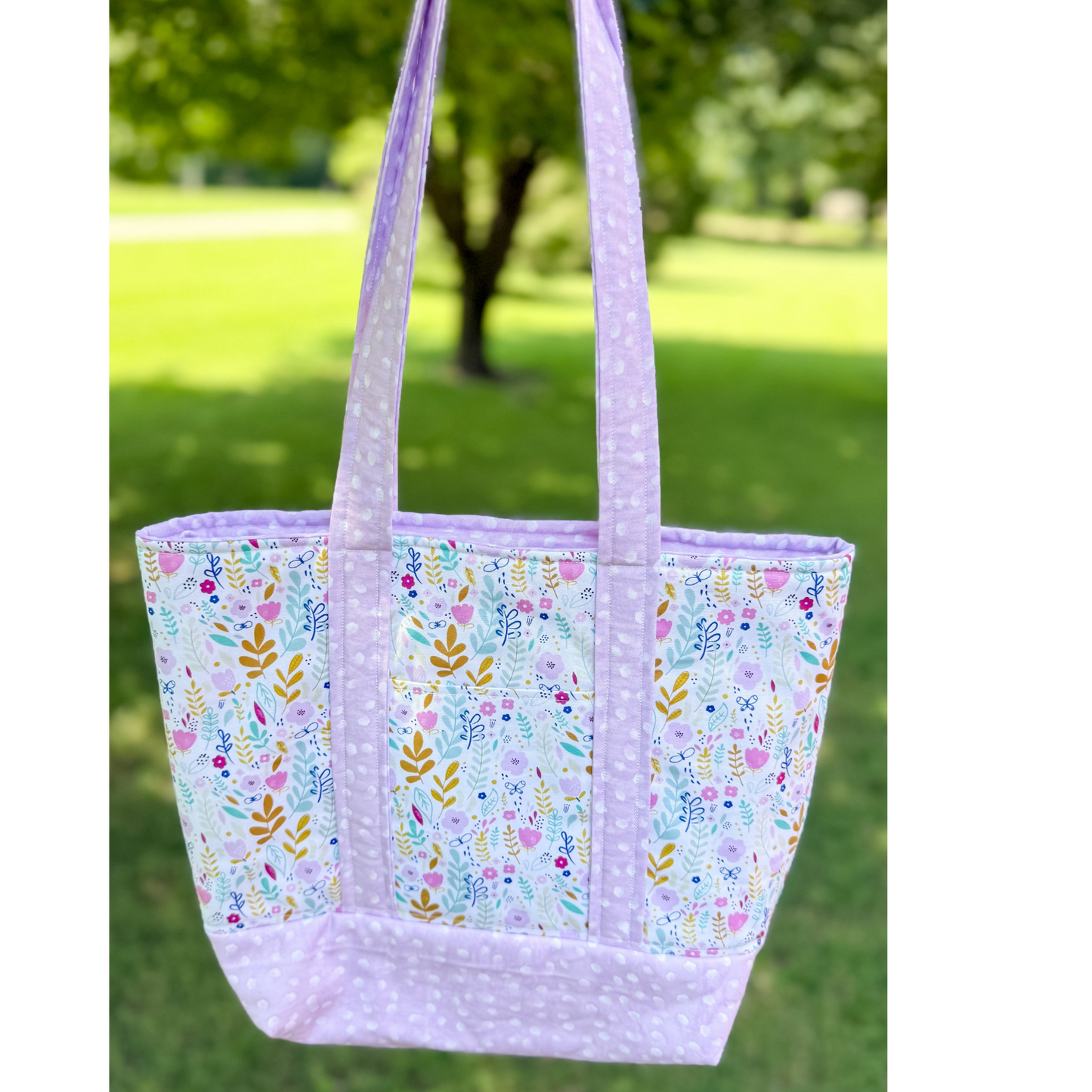 Floral patterned tote bag with purple accents on a grassy background