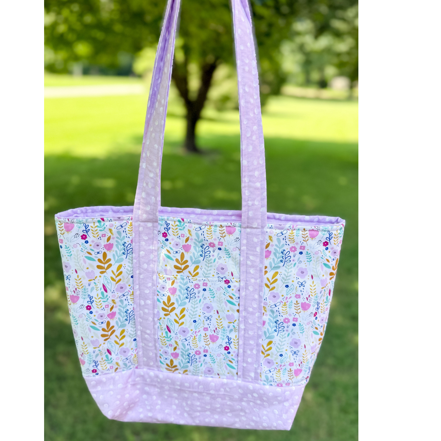 Floral patterned tote bag with purple accents on a grassy background
